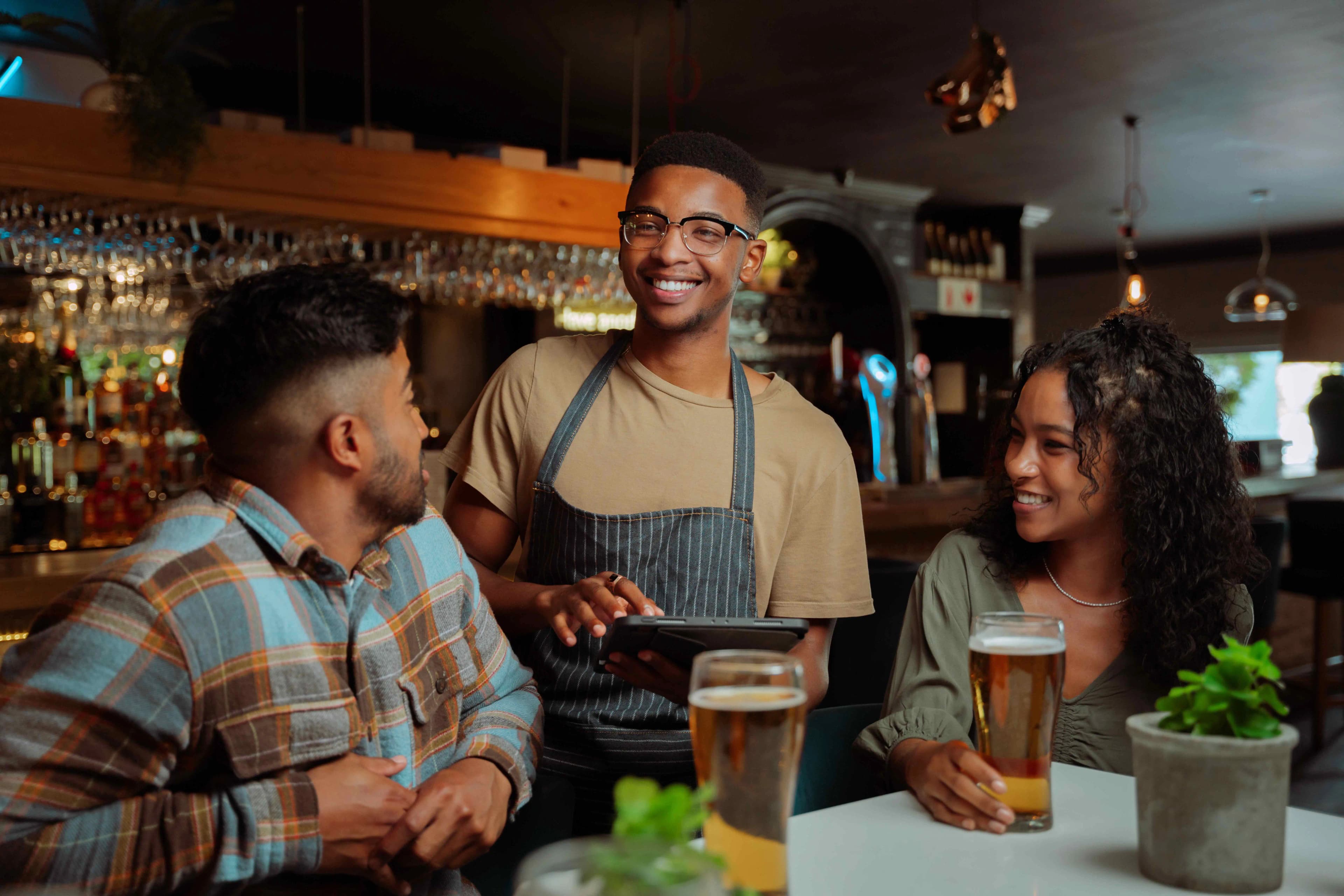 A Rezzr server sharing a moment with two diners at the bar — the everyday ritual of eating out together